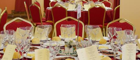 Een banketzaal met gedekte tafels voor een formeel evenement, inclusief kristalglas, borden en menukaarten.