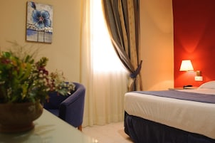 A hotel room with a bed, a desk, a chair, a lamp, and a painting on the wall.