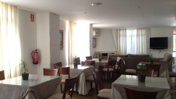 Un comedor de hotel con mesas y sillas, un sofá y un televisor.