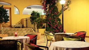 Un espace de restauration en plein air avec des tables et des chaises rondes, un escalier et un mur orné de plantes fleuries.
