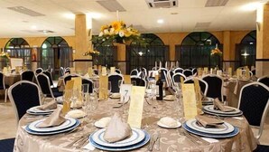 Une salle de banquet avec des tables rondes dressées pour le repas, des menus numérotés et des chaises blanches.