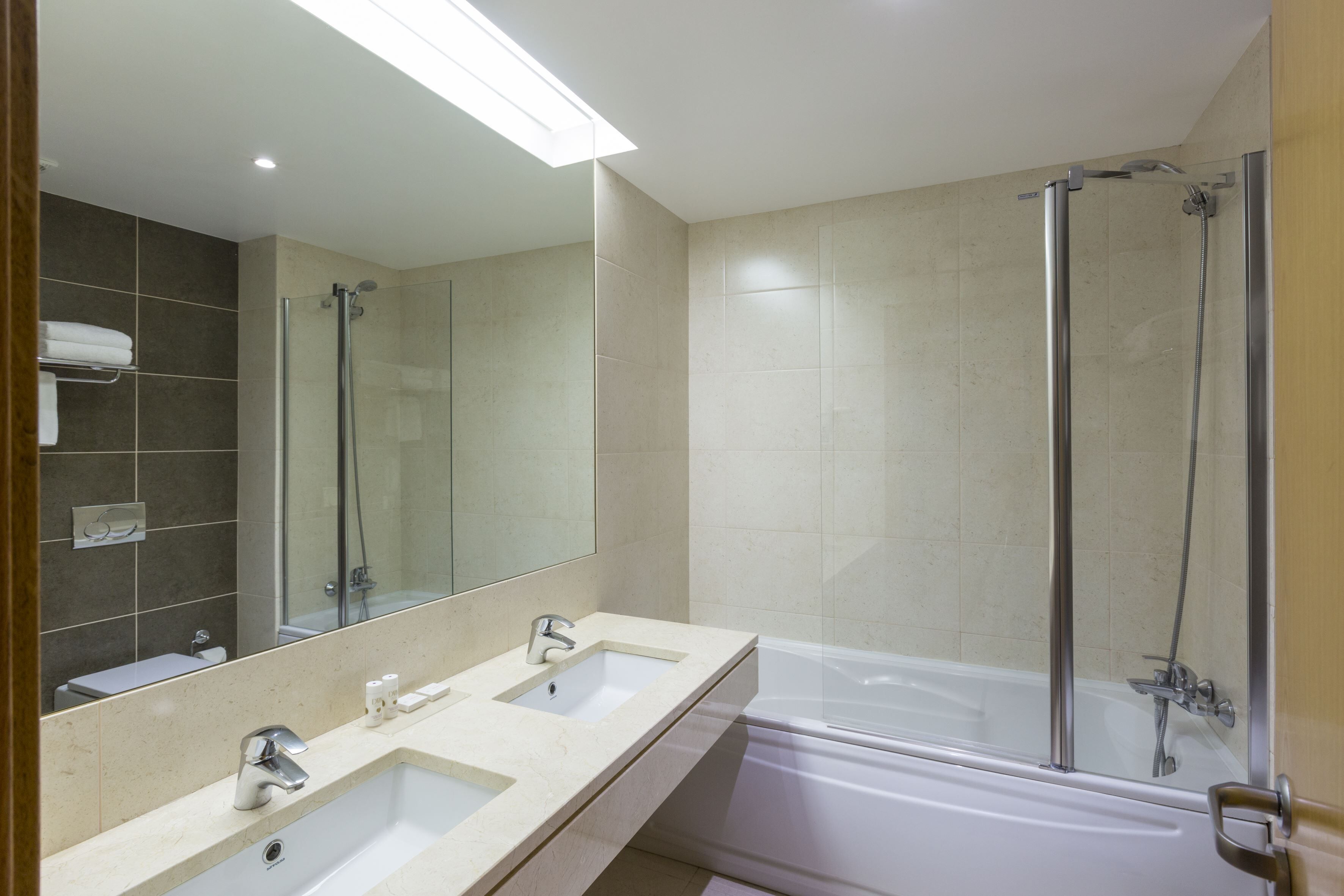 A modern bathroom with two sinks, a large mirror, a glass-enclosed shower, and a bathtub.