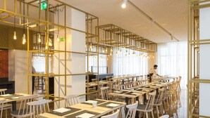 A spacious dining area with multiple tables and chairs, a person serving, and a modern interior design with exposed structural elements and hanging lights. - Hotel Estrela de Fatima (Ourem)
