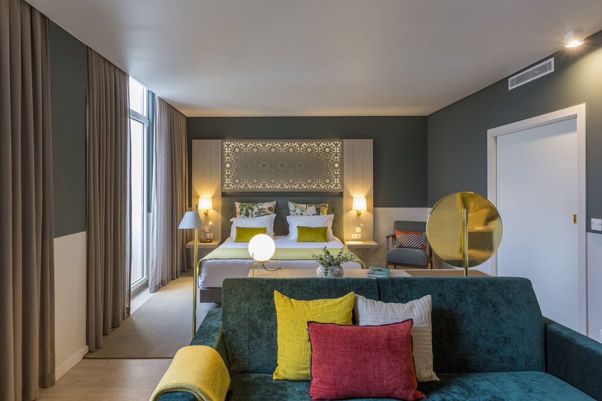 A modern hotel room with a large bed, a green sofa, and a decorative wall panel.