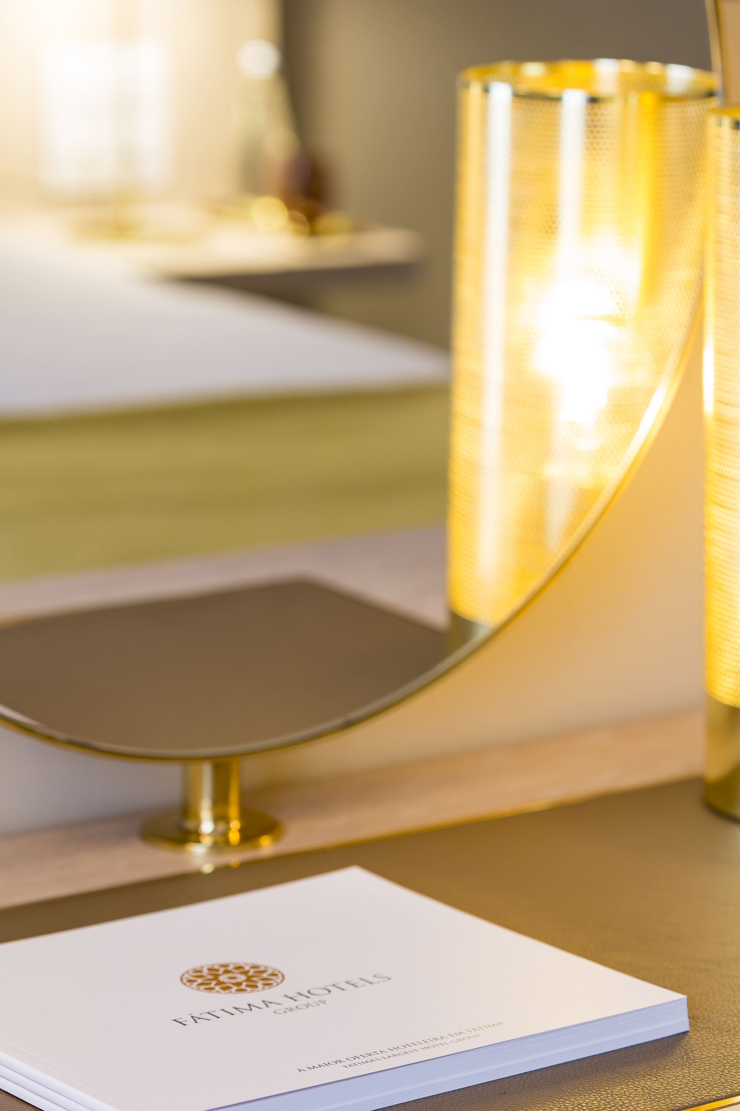 A booklet titled "FÁTIMA HOTEL GROUP" on a table with a gold-colored lamp in the background.