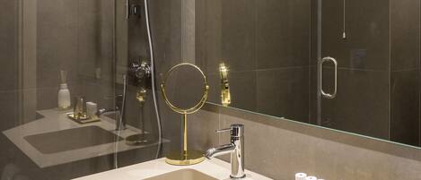 A modern bathroom with a large mirror, a shower, and a vanity with a sink and toiletries.