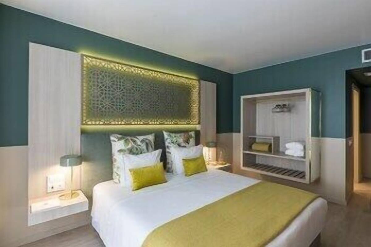 A modern hotel room with a bed, bedside tables, a built-in wardrobe, and a decorative wall panel.
