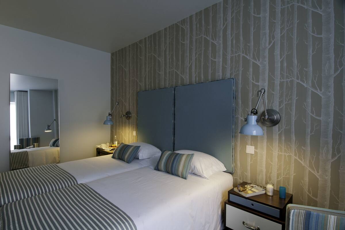 A hotel room with a large bed, two bedside tables, a nightstand, a mirror, and a wall with a tree pattern.