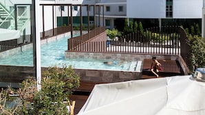 A rooftop pool area with a hot tub, wooden deck, and a view of a modern building. - Hotel Estrela de Fatima (Ourem)