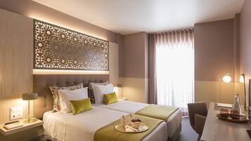 Habitación de hotel con dos camas, un escritorio, un panel decorativo en la pared y un ventanal con cortinas.