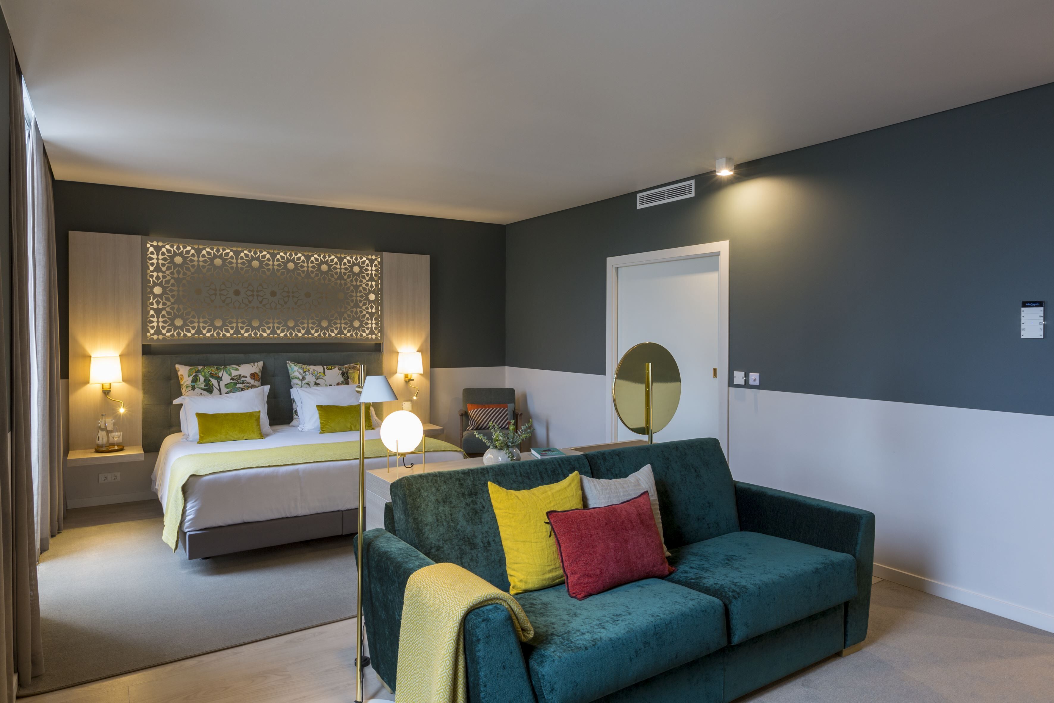 A modern bedroom with a bed, a green sofa, and a bedside table with a lamp.