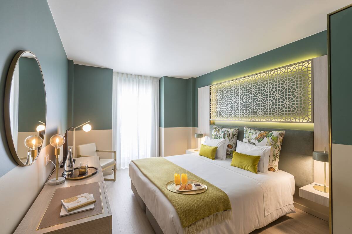 A modern hotel room with a large bed, bedside tables, a mirror, and a decorative headboard.