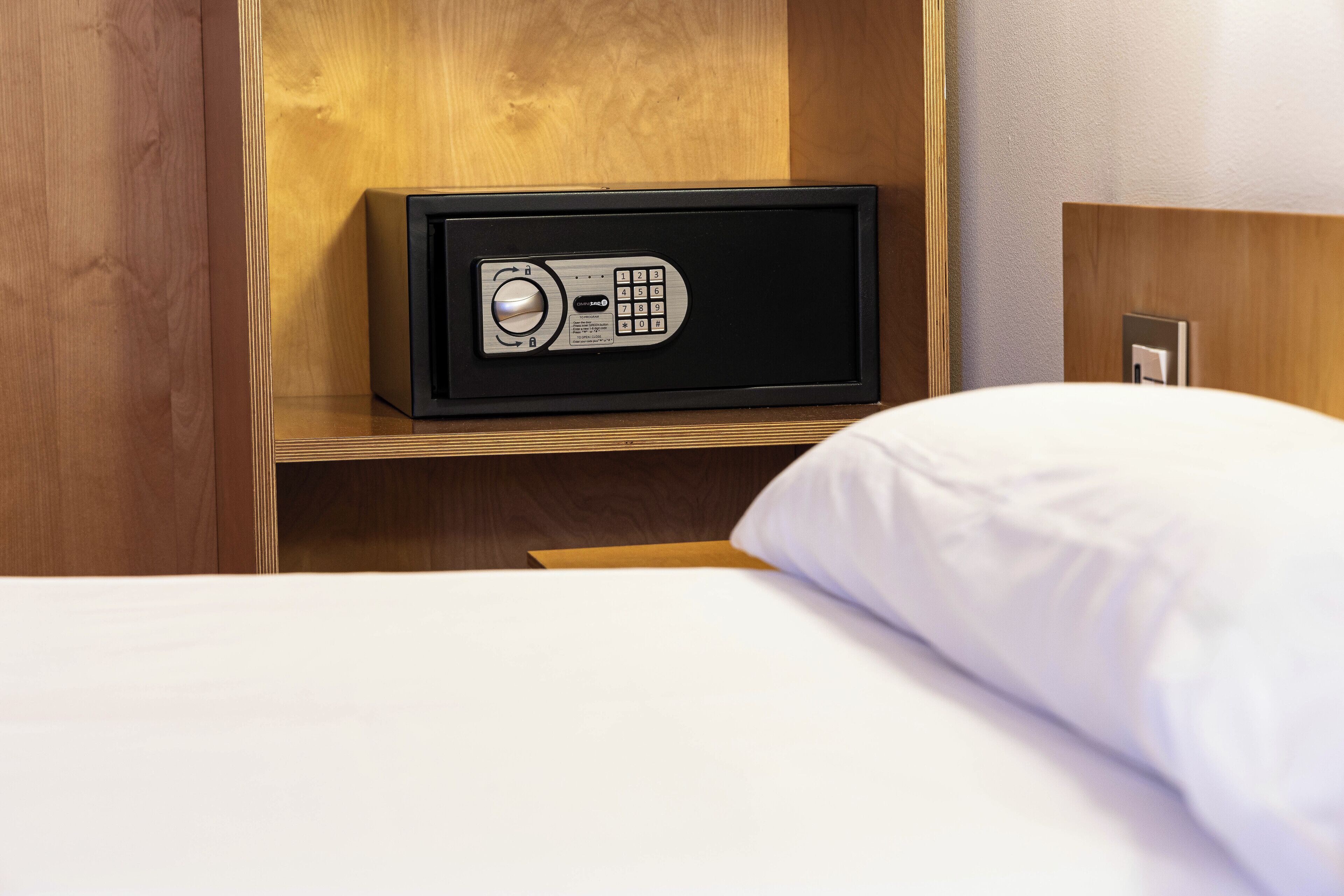 Une chambre d’hôtel avec un lit, une tête de lit en bois et un coffre-fort placé sur une étagère.