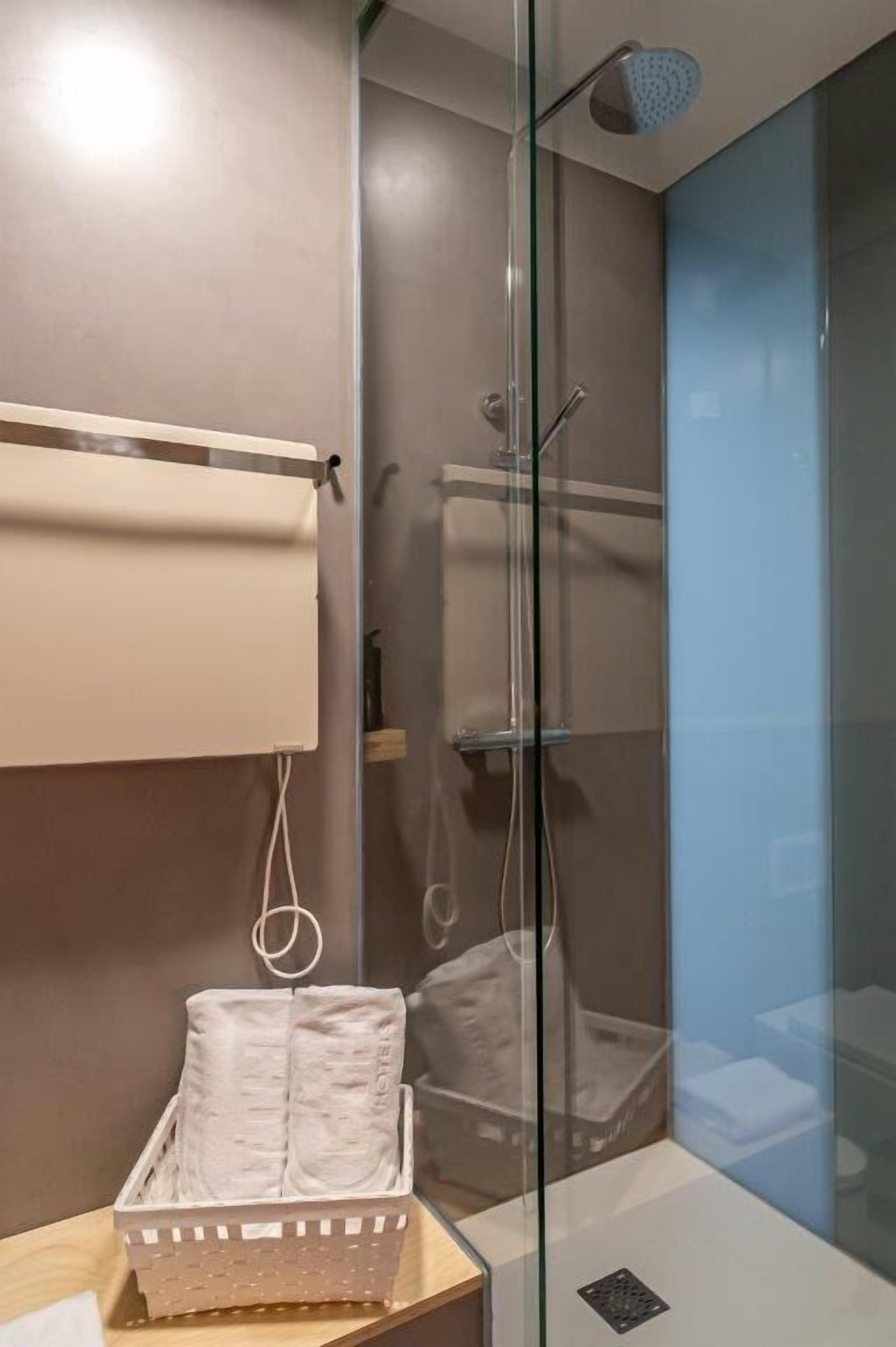 Un baño moderno con cabina de ducha de vidrio, un perchero y un cesto de toallas.