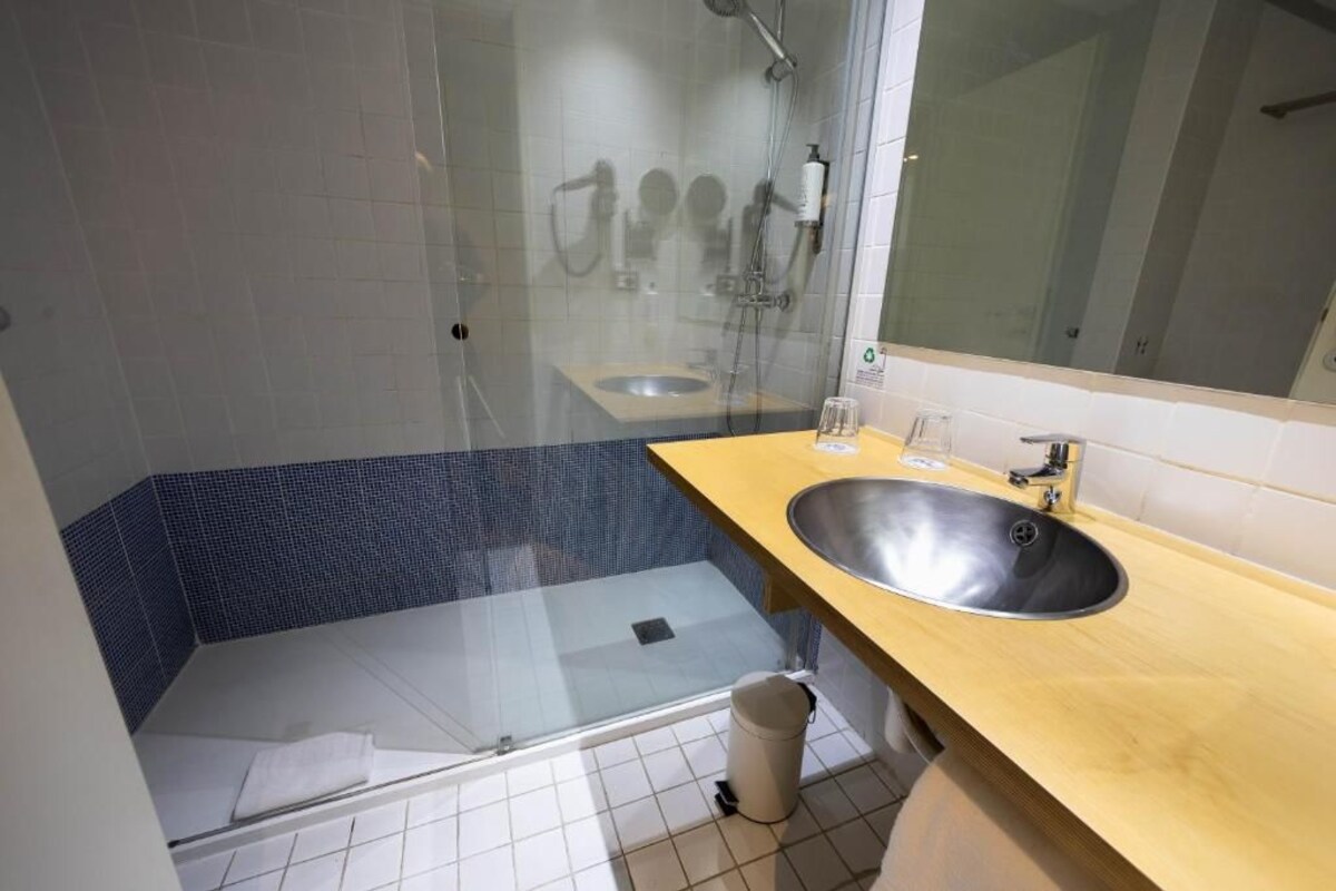 Un baño con ducha envuelta en vidrio, un lavamanos y un espejo.