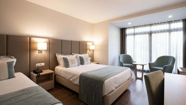 A hotel room with two beds, a desk, a chair, and a small table.