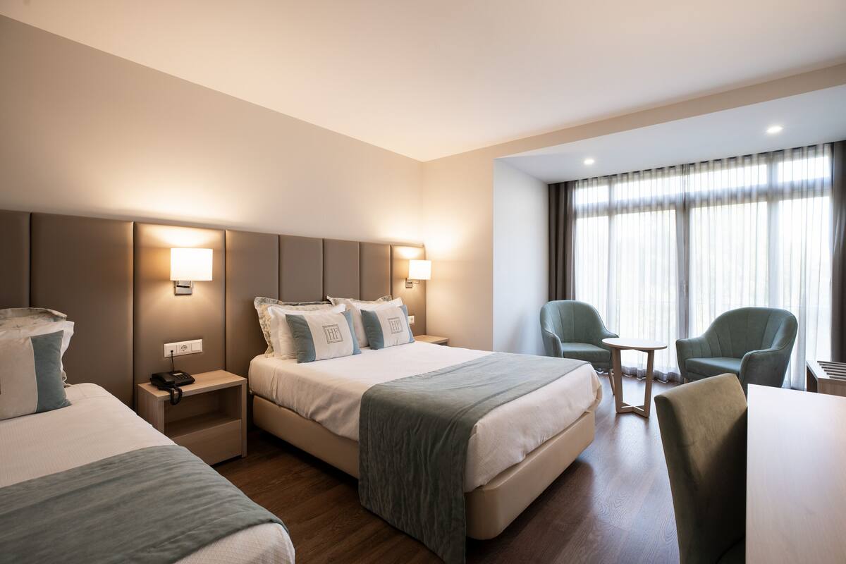 Quarto de hotel com duas camas, uma escrivaninha, uma cadeira e uma pequena mesa.
