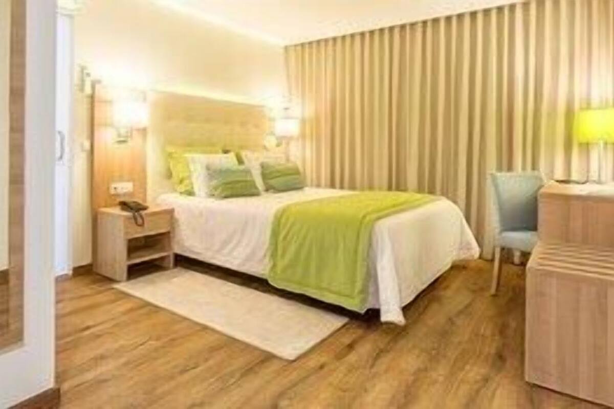 Quarto de hotel com cama, mesa de cabeceira, abajur e uma cadeira.