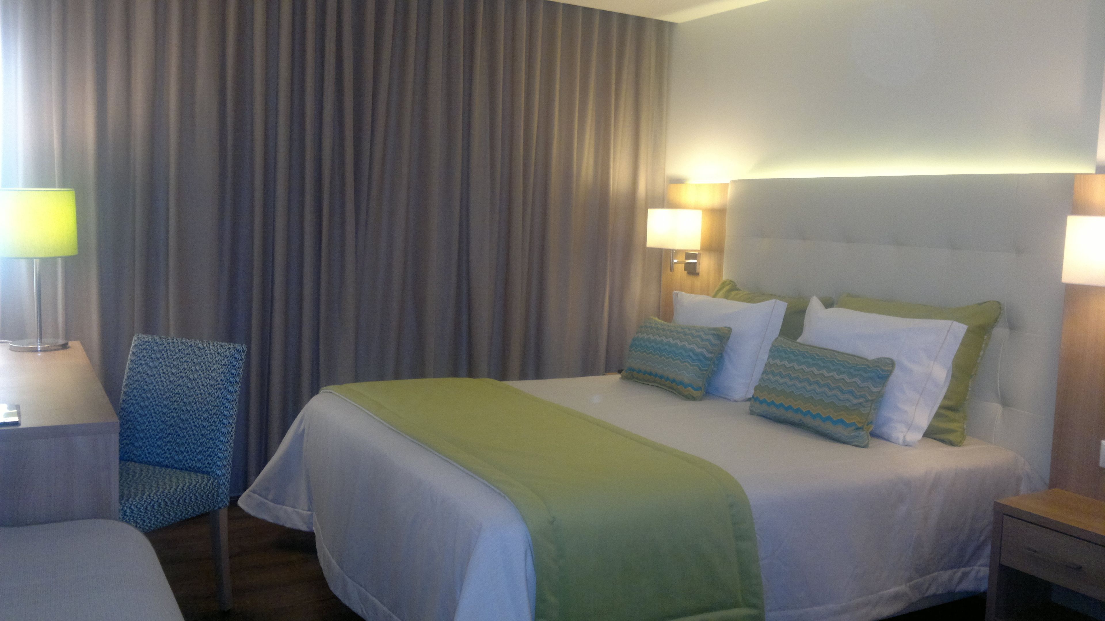 Una habitación de hotel con cama, una silla, un escritorio y una lámpara.