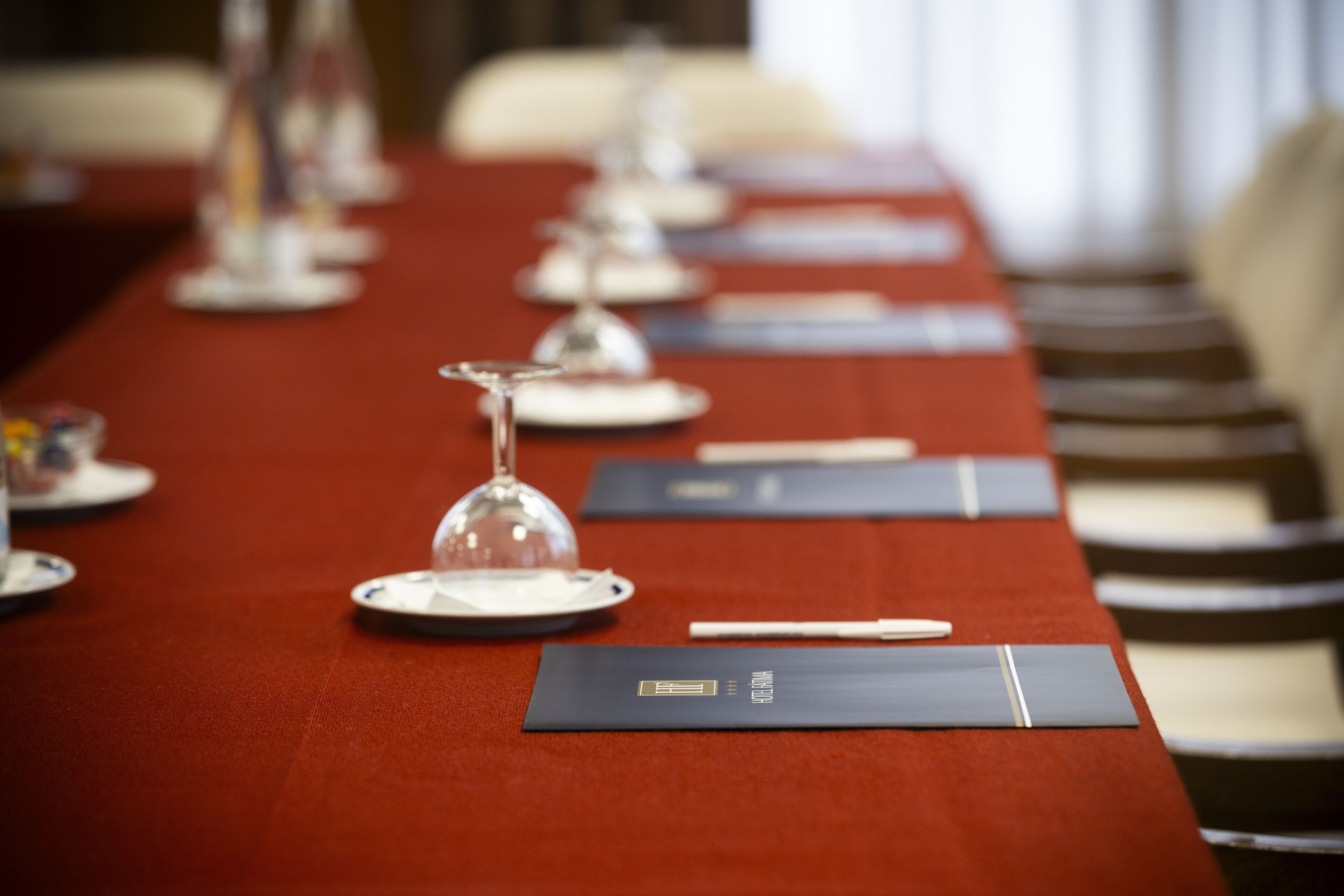 A conference table with a red tablecloth, glassware, and folders.
