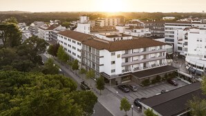 Un edificio de varios pisos con techo plano, rodeado de árboles y otros edificios.