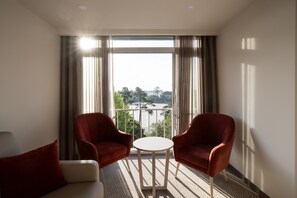 A hotel room with a balcony, two red armchairs, a small round table, and a view of a cityscape. - Hotel Fatima (Ourem)