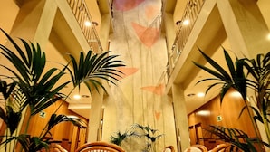 A spacious atrium with a high ceiling, featuring a central staircase, multiple seating areas with wicker furniture, and potted plants. - Hotel Flor Parks (Barcelona)