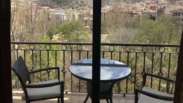 Un balcó amb una taula rodona i dues cadires, amb vista a una vila amb edificis i un turó.