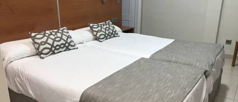 Una cama doble con cabecera de madera, dos almohadas estampadas, una colcha gris y una mesita de noche con lámpara.