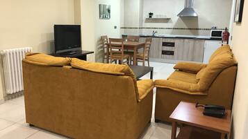 Una sala de estar con sofá y televisión, un comedor con sillas, y una cocina con estufa y microondas.