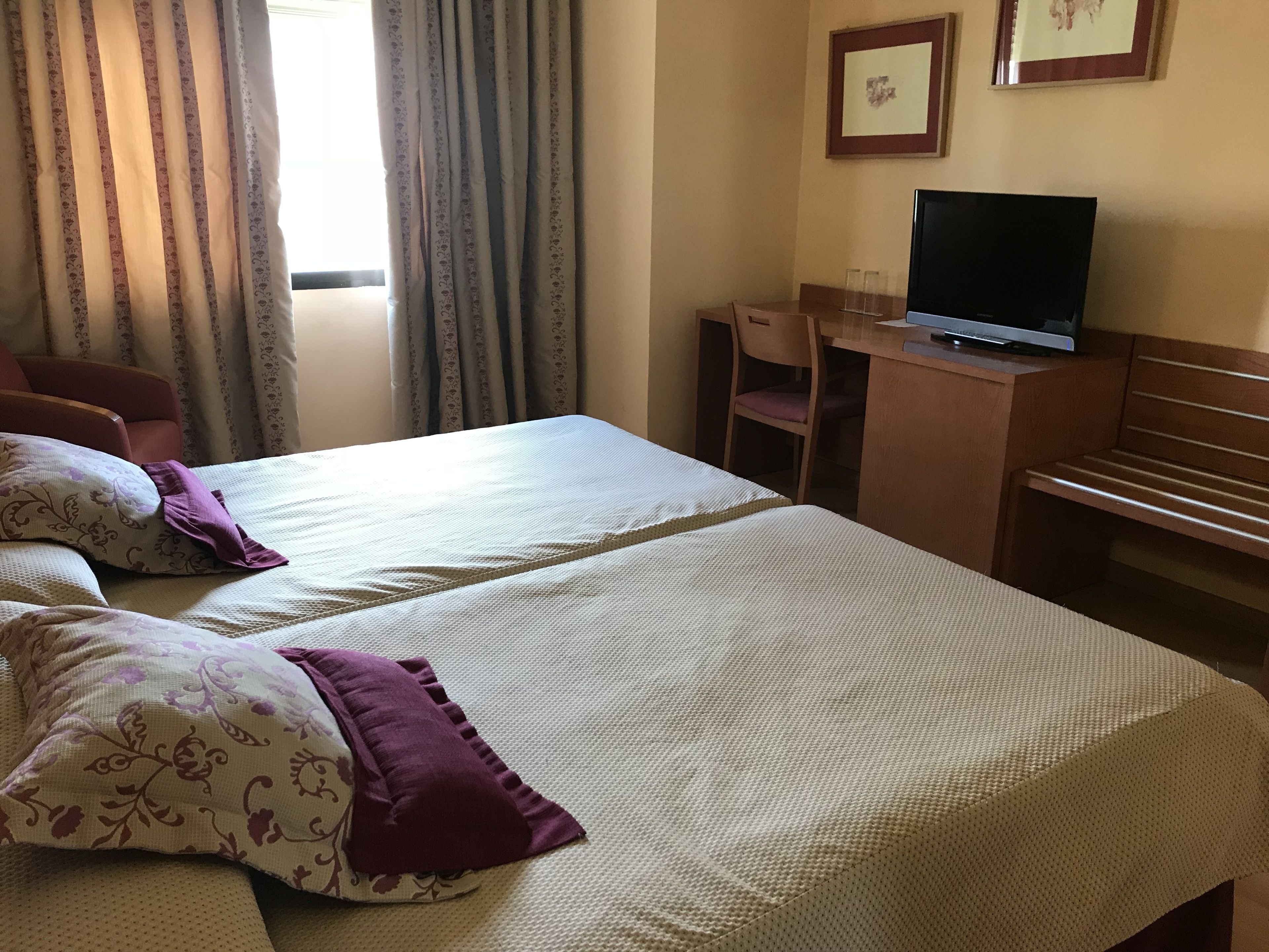 A hotel room with two beds, a desk with a television, and a chair.