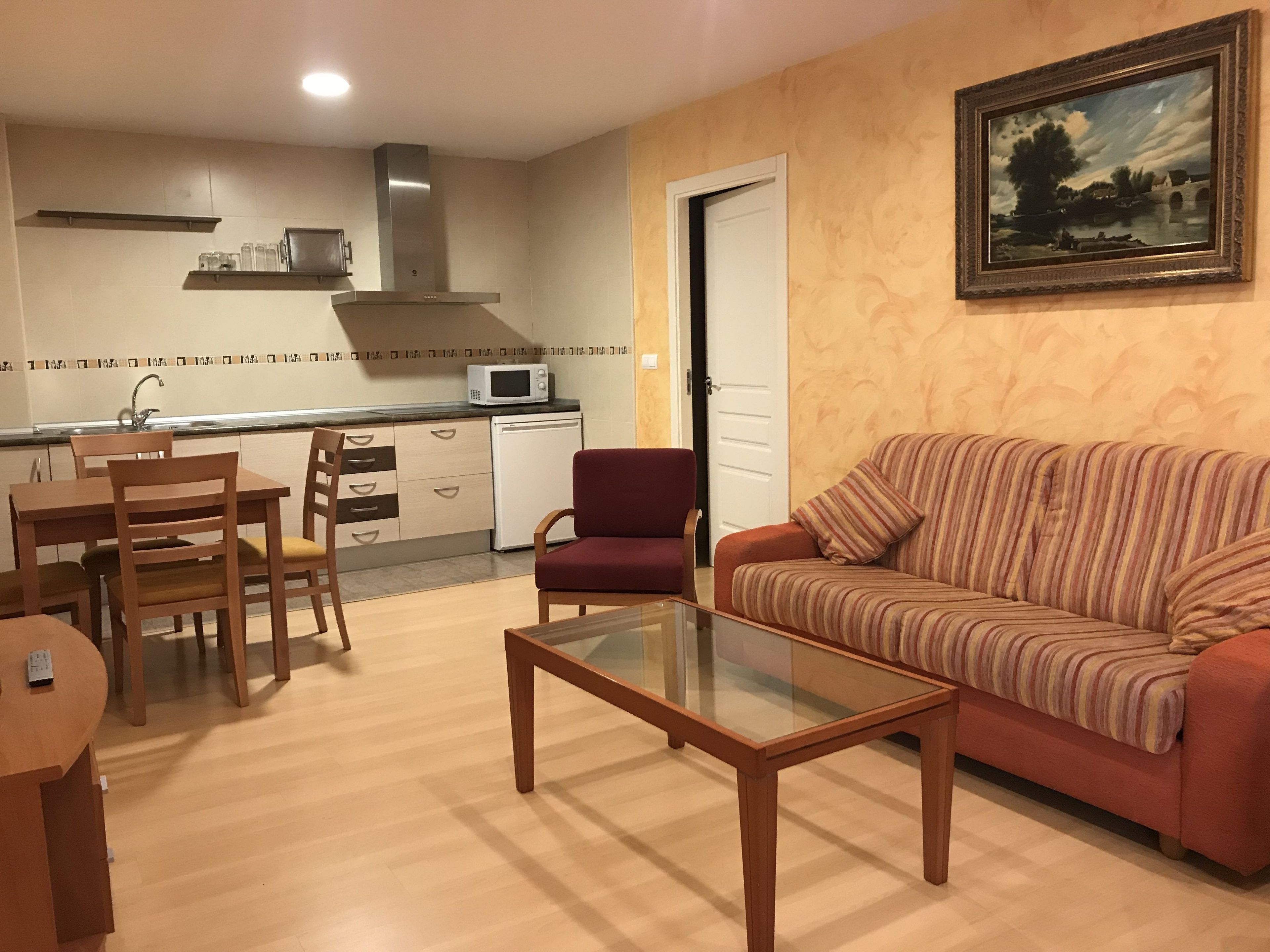 Un salon comprenant un canapé, une table basse en verre, une table à manger avec des chaises, un four à micro-ondes et un petit coin cuisine avec des placards et un évier.