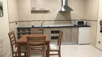 Una cocina compacta con una mesa de comedor, sillas, microondas, lavamanos y un refrigerador pequeño.