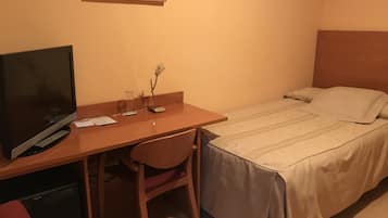 A hotel room with a wooden desk, a television, a chair, a bed with a white bedspread, and a framed picture on the wall.