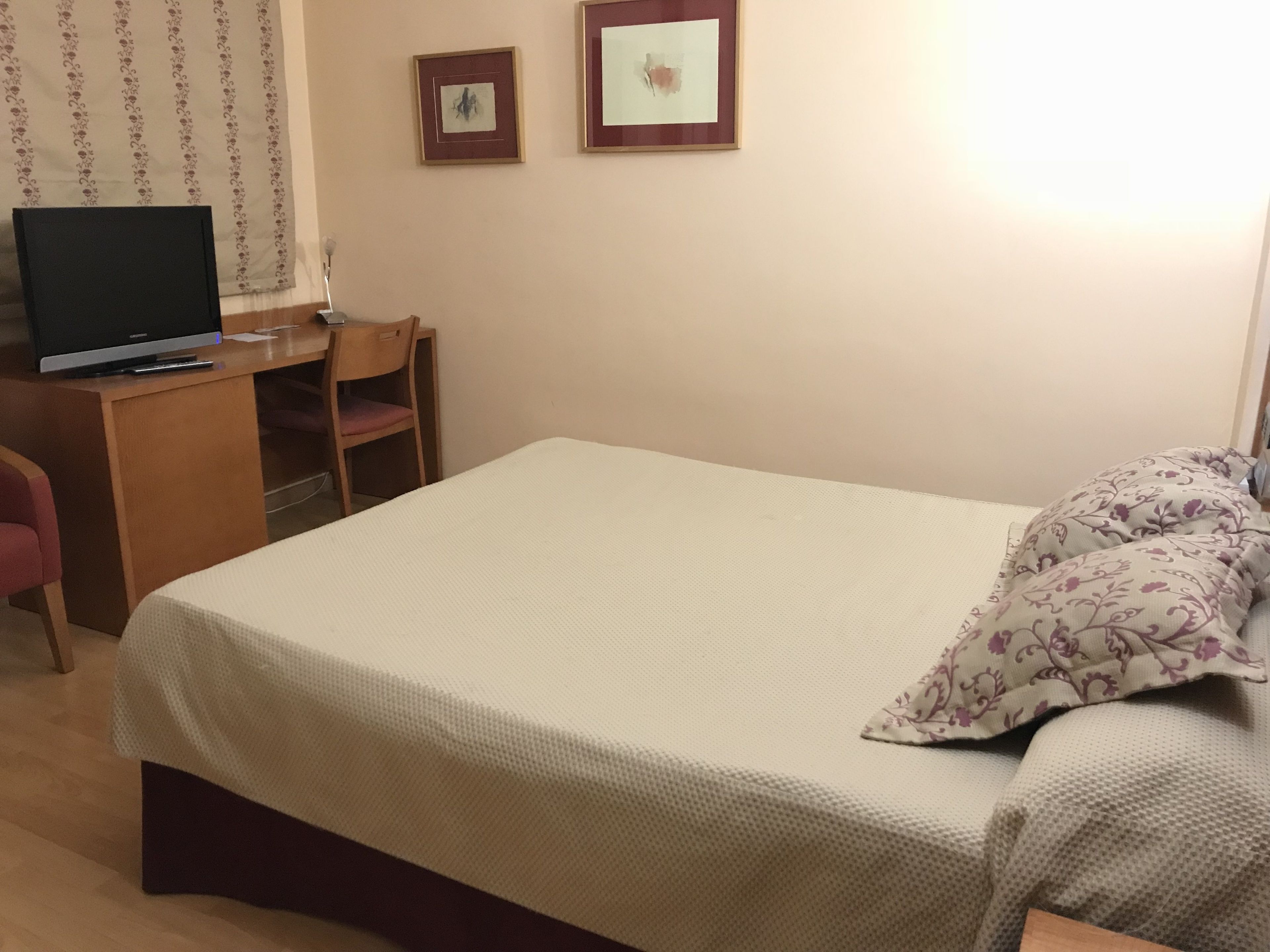 Un dormitorio con cama, un escritorio con computadora, una silla y dos cuadros en la pared.