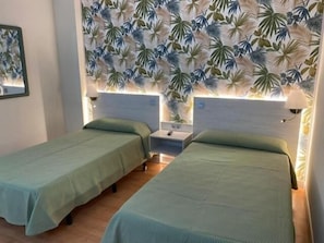 Una habitación con dos camas individuales, cada una con colcha verde, un mesita de noche y una lámpara de pared.