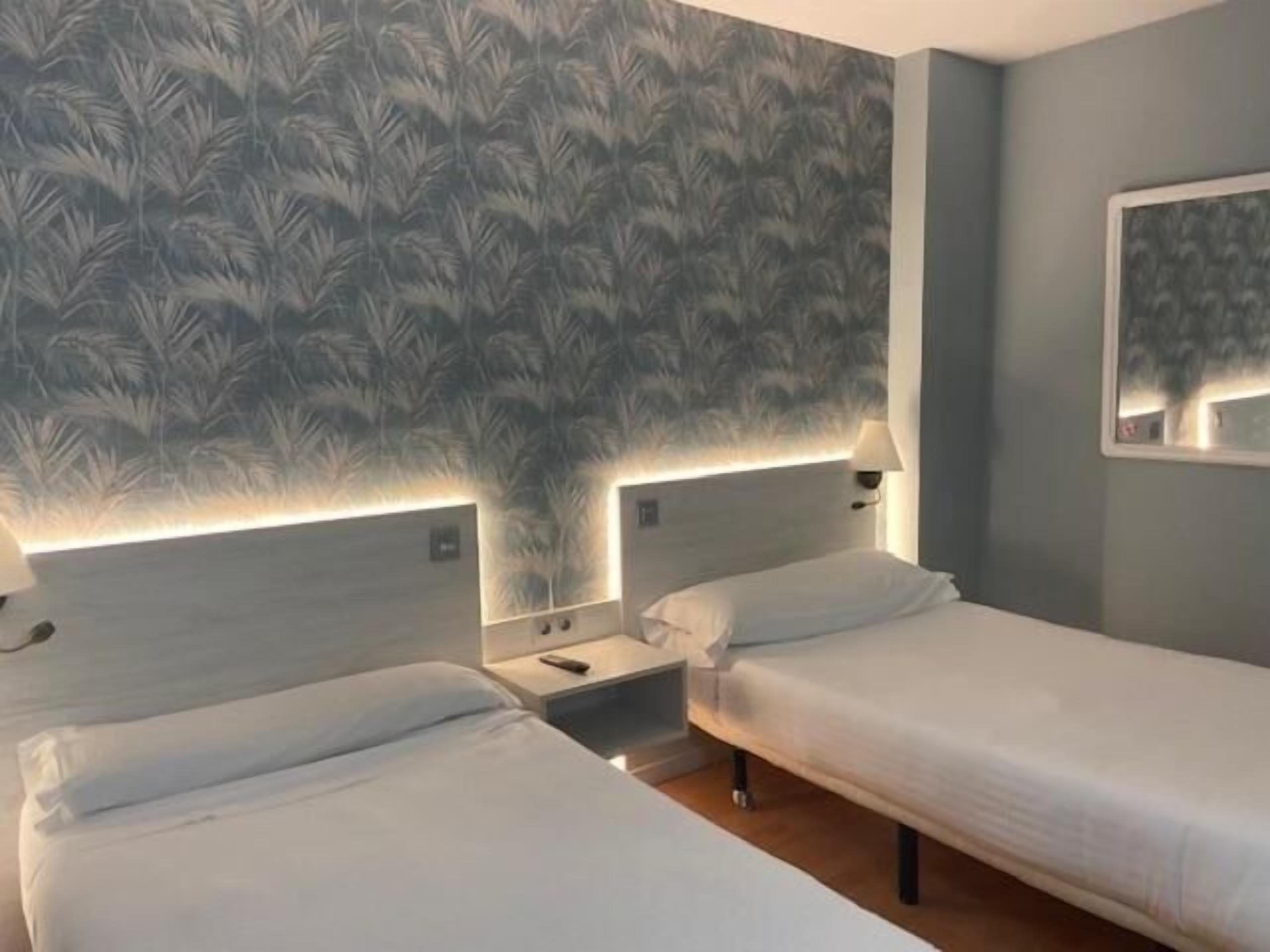 Habitación de hotel con dos camas, una mesita de noche y una lámpara de pared.
