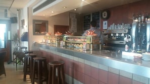 Una zona de bar con taburetes, una barra con exhibición de alimentos y una máquina de café.