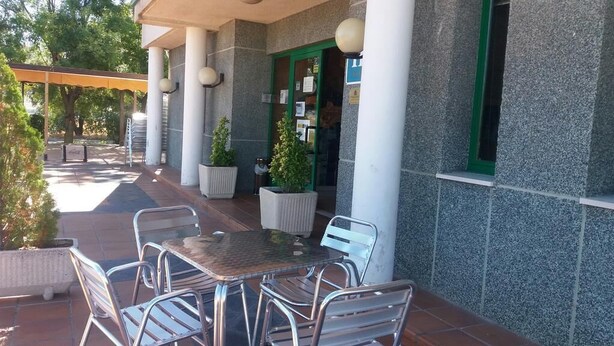 An outdoor patio with metal chairs and a table, surrounded by potted plants and a covered area. - Miralcampo (AZUQUECA DE HENARES)