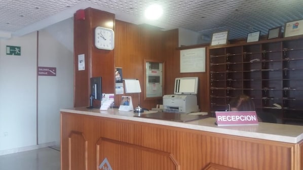 Una reception con una scrivania, un orologio, un cartello che riporta la scritta "RECEPCION" e un monitor per computer.