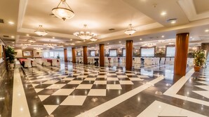 Un amplio vestíbulo de hotel con suelo a cuadros, múltiples candelabros y filas de mesas dispuestas para eventos.