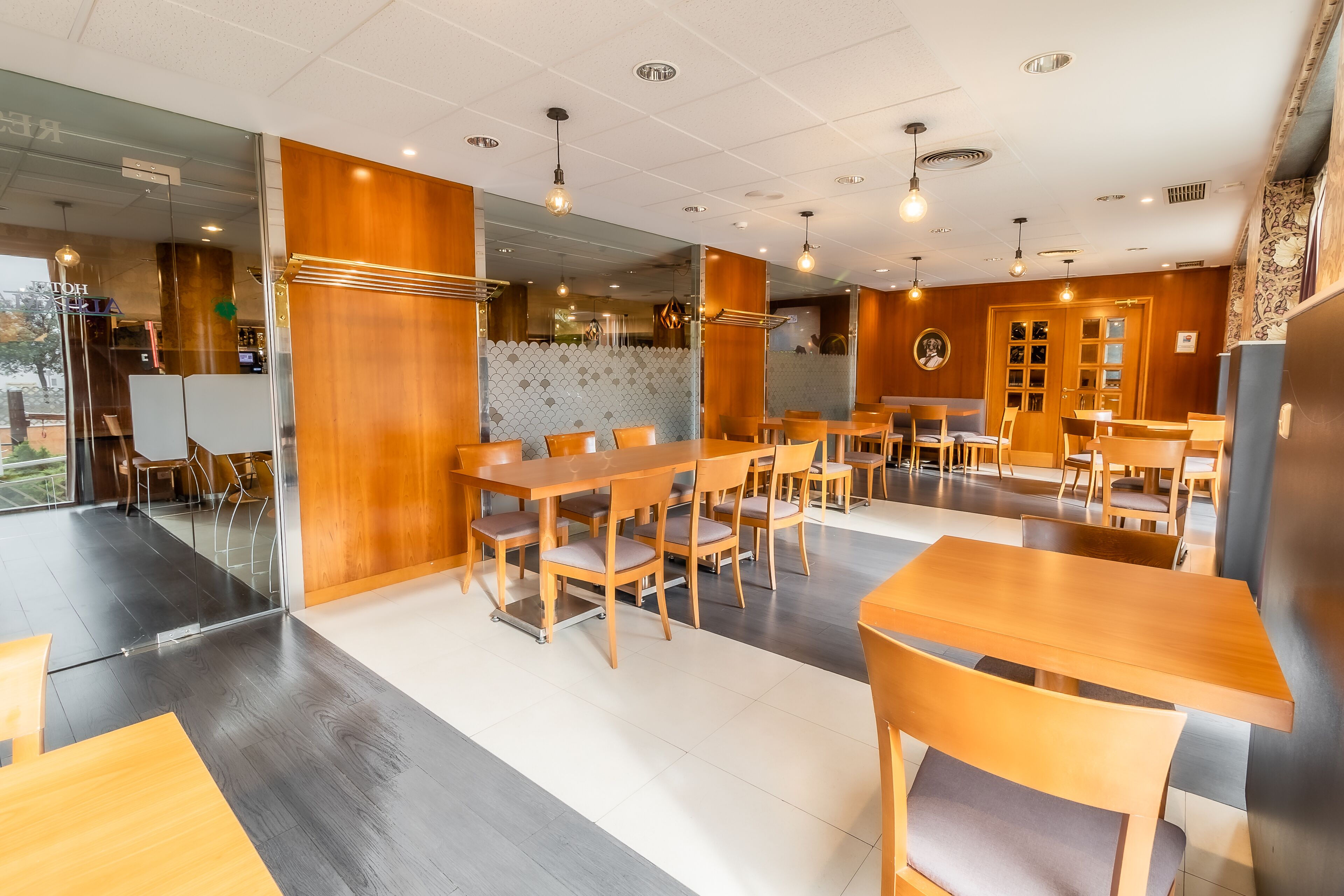 Ein modernes Restaurant mit Holztischen und -stühlen, einem Fliesenboden und einer Glaswand.