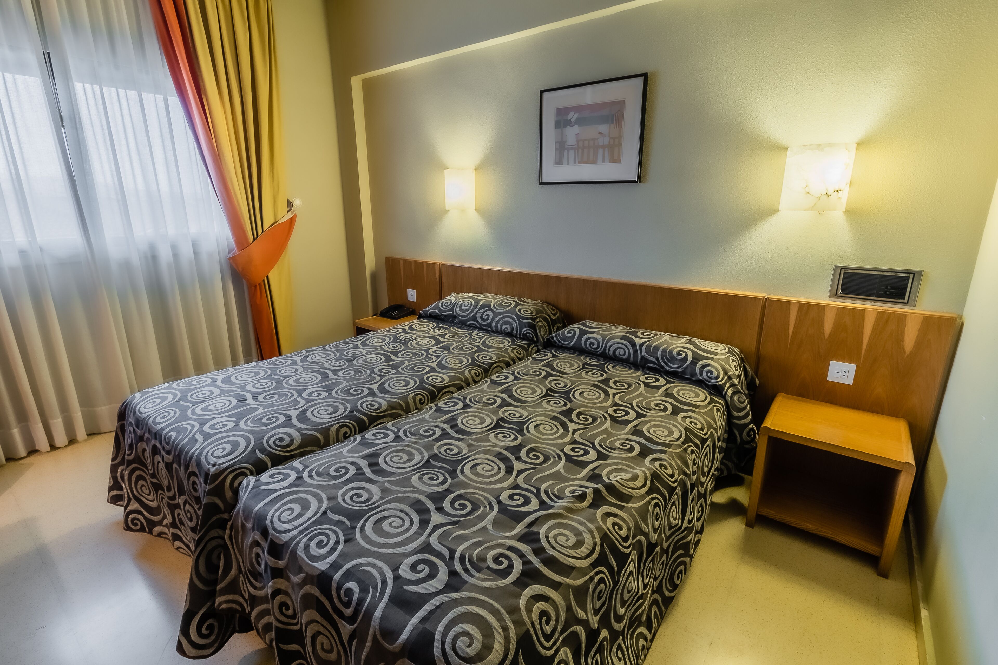 A hotel room with a double bed, two bedside tables, a nightstand, and a wall-mounted light fixture.