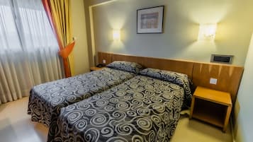 A hotel room with a double bed, two bedside tables, a nightstand, and a wall-mounted light fixture.