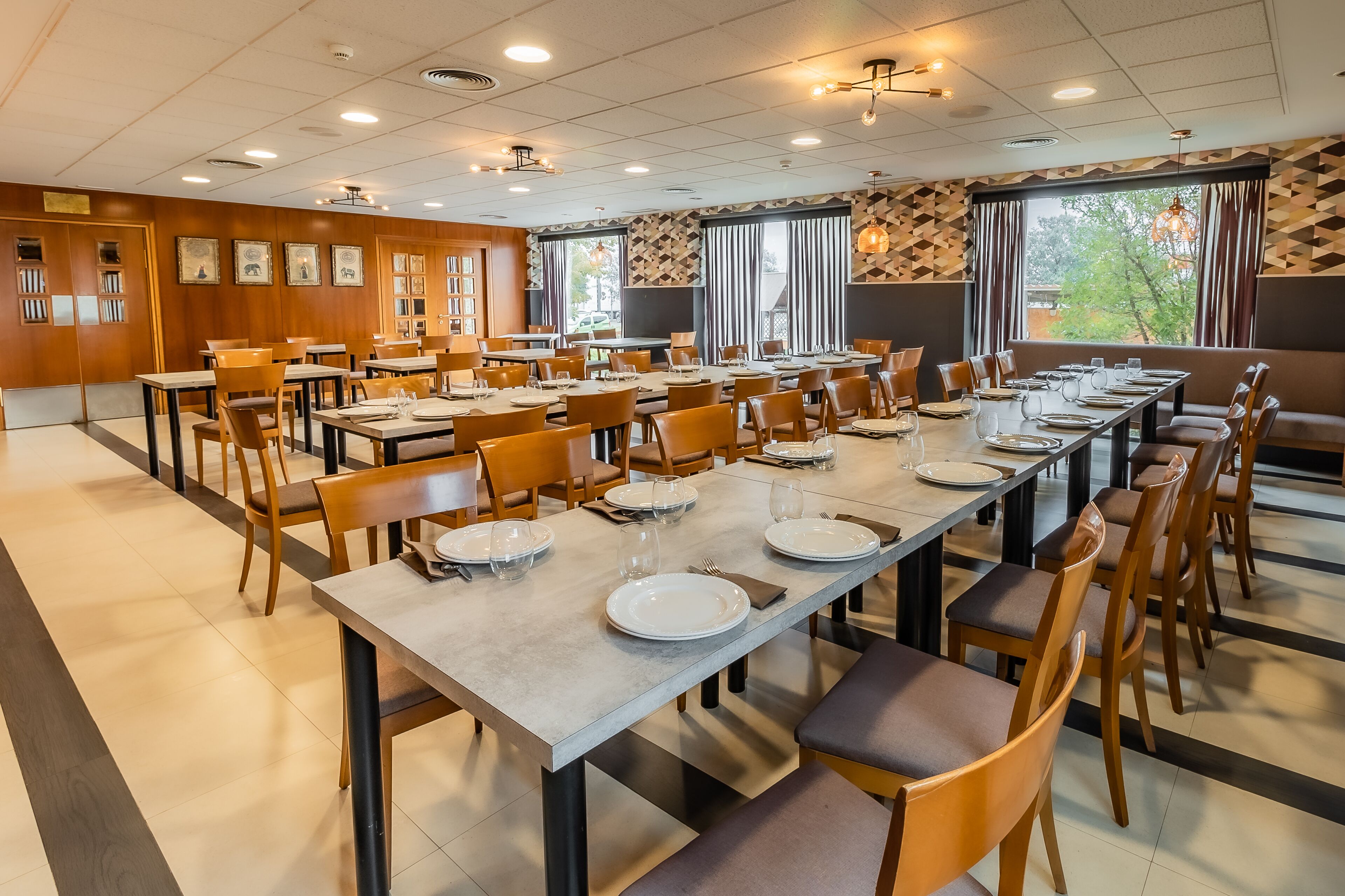 Un comedor amplio con varias mesas dispuestas para comidas, sillas de madera y vistas a árboles a través de amplios ventanales.