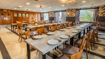 Un comedor amplio con varias mesas dispuestas para comidas, sillas de madera y vistas a árboles a través de amplios ventanales.