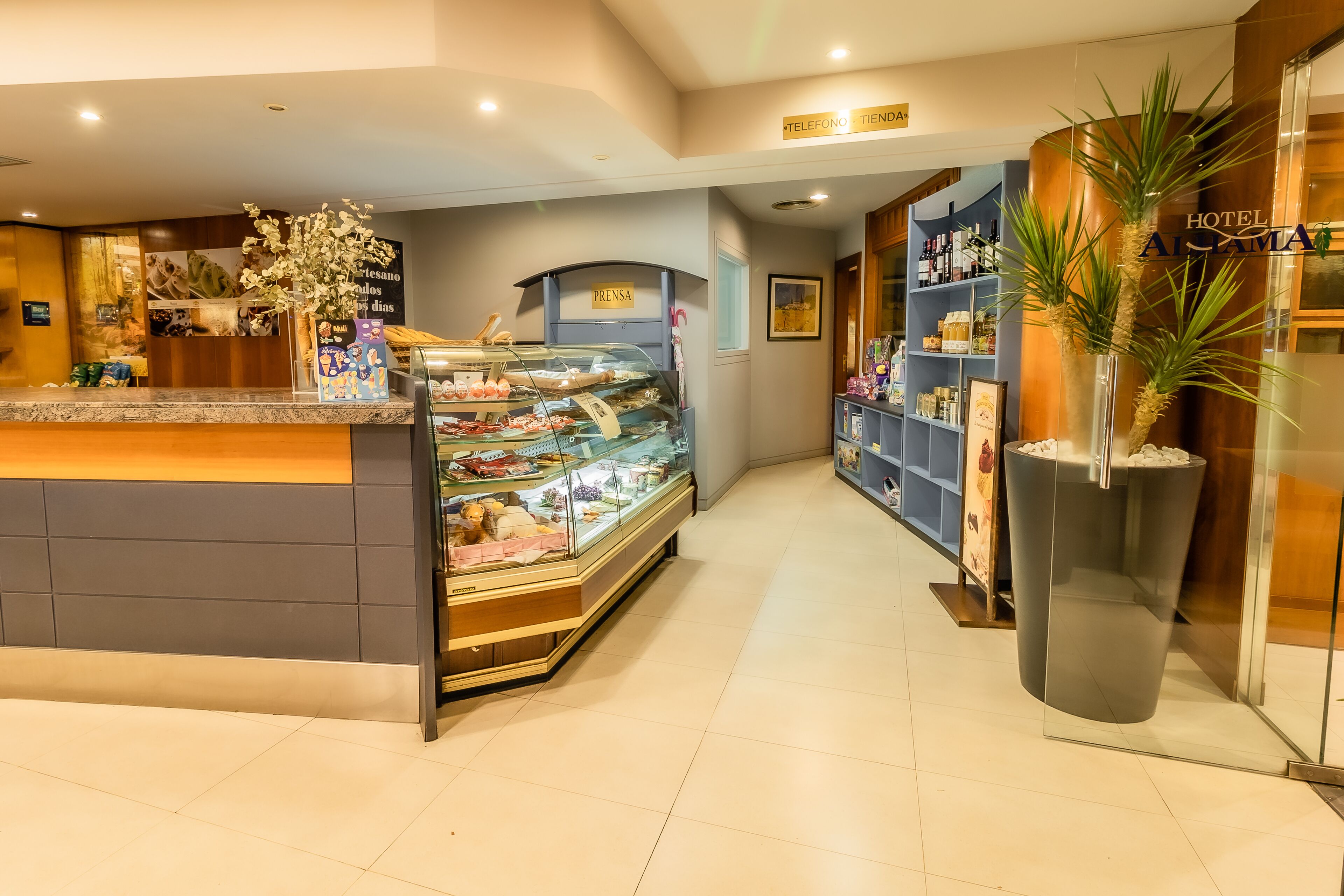 A hotel reception area with a glass display case of pastries, a reception desk, and a minibar.