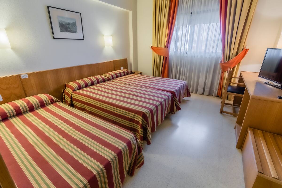 A hotel room with three single beds, a wooden desk with a television, and a chair.