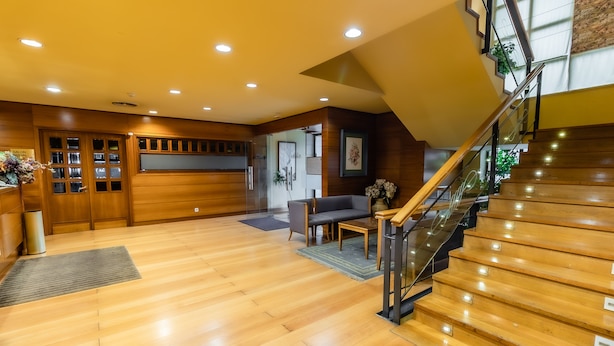 Un vestíbulo amplio con suelo de madera, una escalera y una recepción con mostrador y plantas.