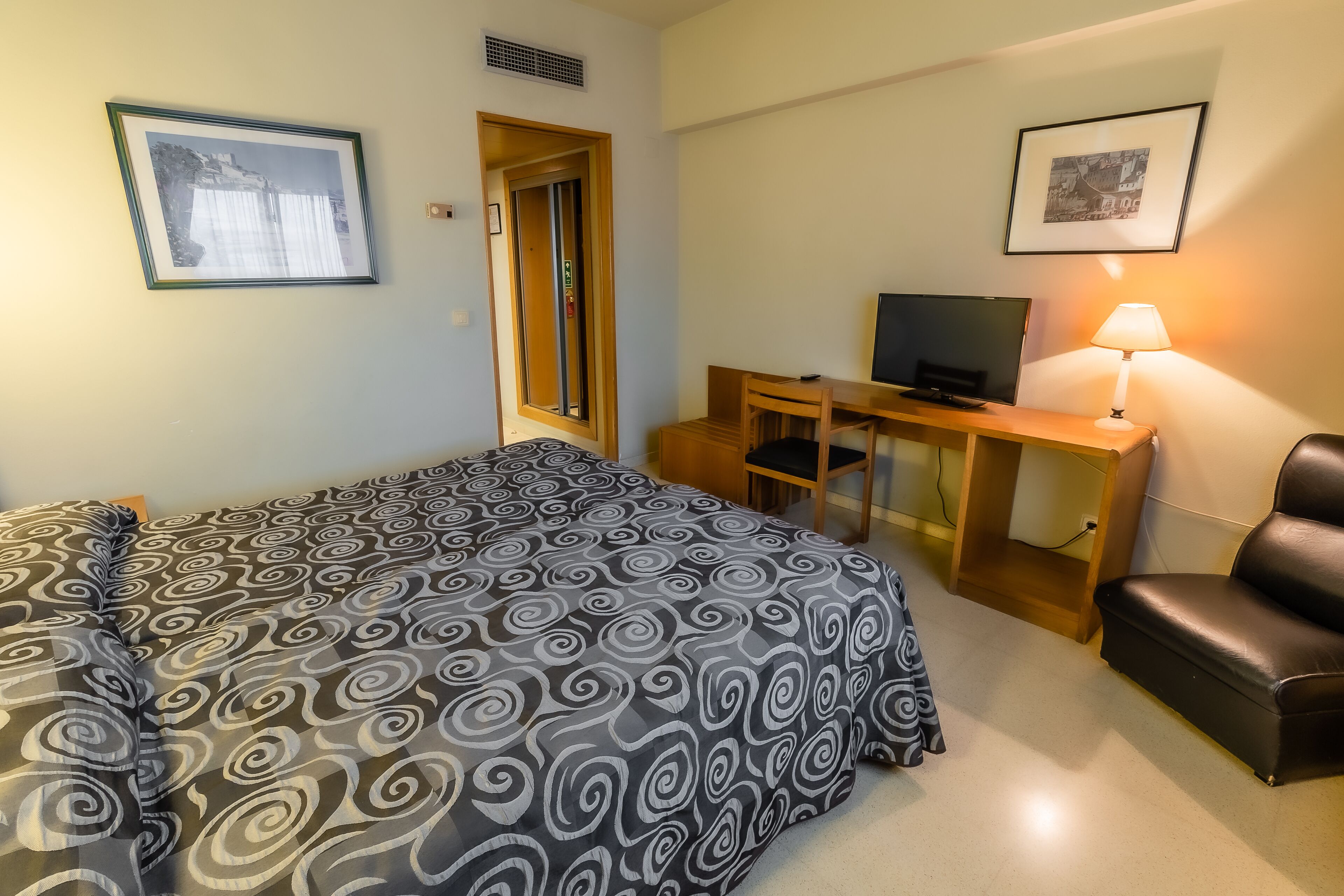 Una habitación de hotel con una cama, un escritorio con televisor, una silla y una lámpara.